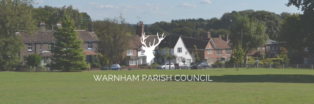 View of old Warnham houses from from the green with white stag logo and "Warnham Parish Council" written over top